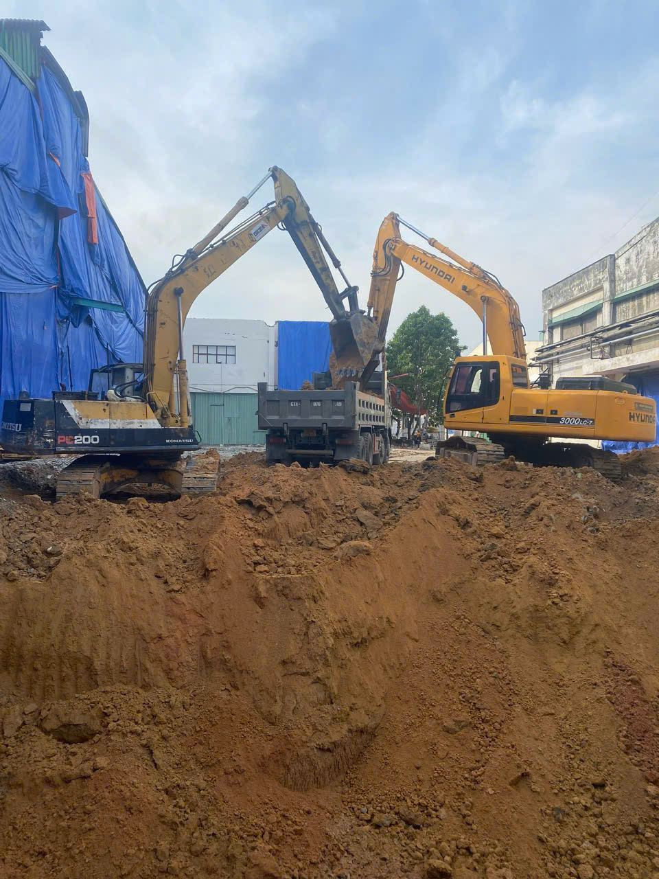 Nhiều máy đào và xe tải hoạt động trên sân bãi rộng của nhà xưởng quy mô lớn