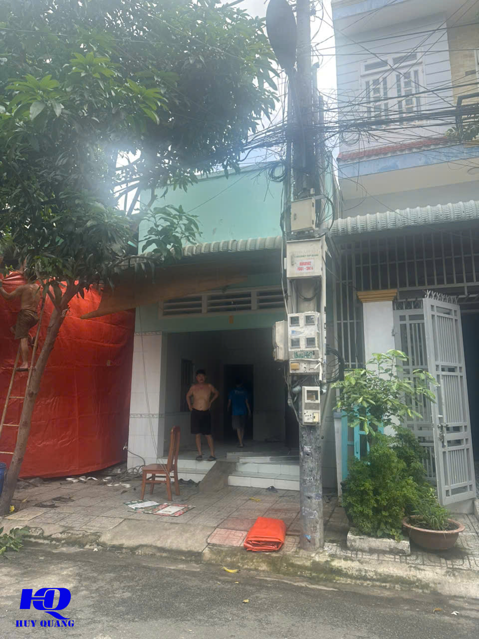 Công nhân che chắn mặt tiền công trình nhà phố bằng bạt màu cam trước khi phá dỡ, hai người đứng bên trong khu vực đã dọn trống chuẩn bị thi công