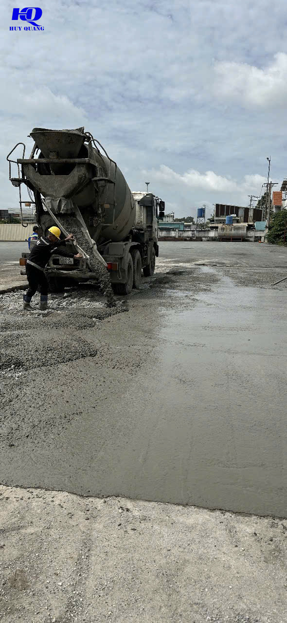 Đống bê tông vụn lẫn cốt thép uốn cong sau khi đục phá, đầu gắp thủy lực của máy đào chờ sẵn bên cạnh nhà xưởng tường tôn