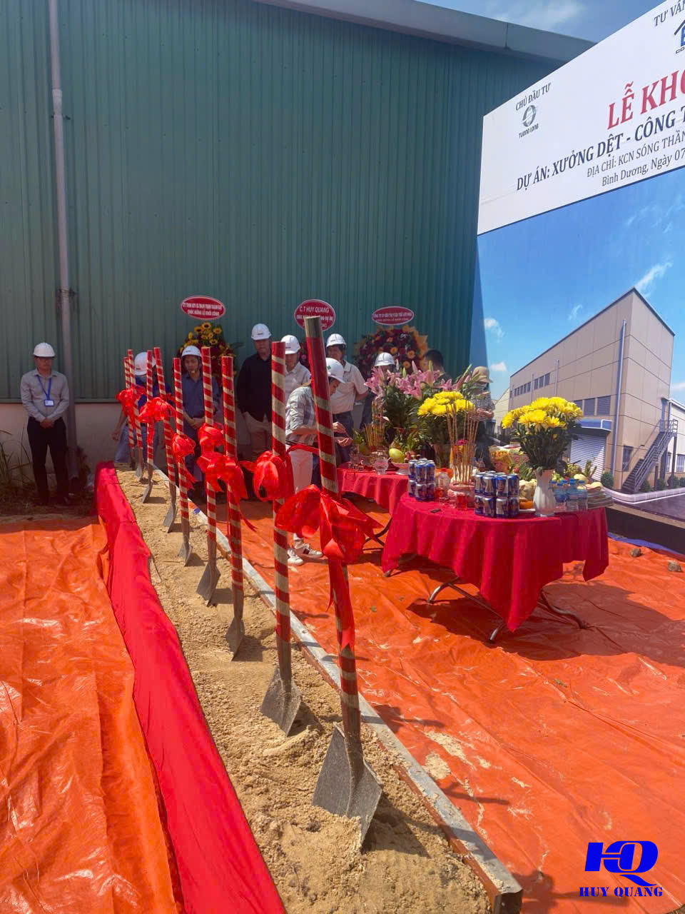 Lễ khởi công dự án xưởng dệt, hàng xẻng cắm trên nền cát phủ bạt cam, băng-rôn ghi tên chủ đầu tư và địa chỉ KCN Sóng Thần