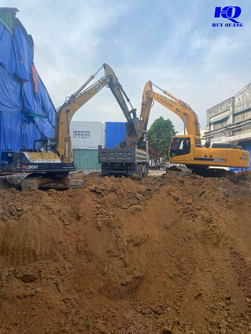 Máy đào Komatsu PC200 và Hyundai 300LC-7 xúc đất lên xe ben tại công trình cạnh nhà xưởng