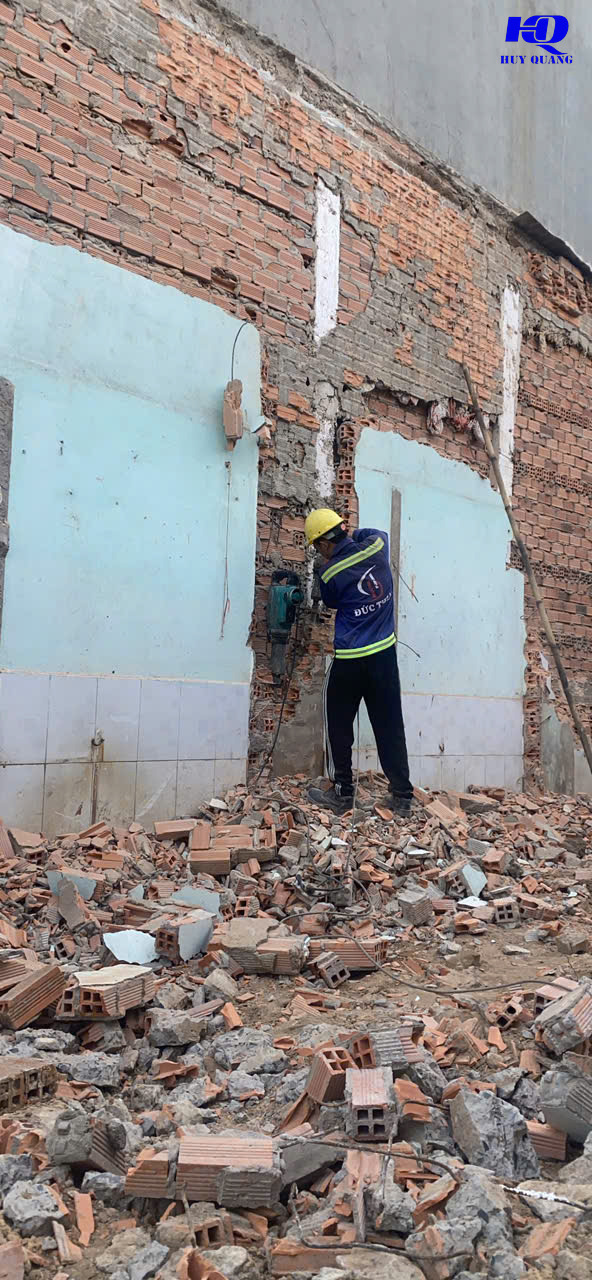 Công nhân đội mũ bảo hộ và áo phản quang đục phá tường gạch bằng máy cầm tay