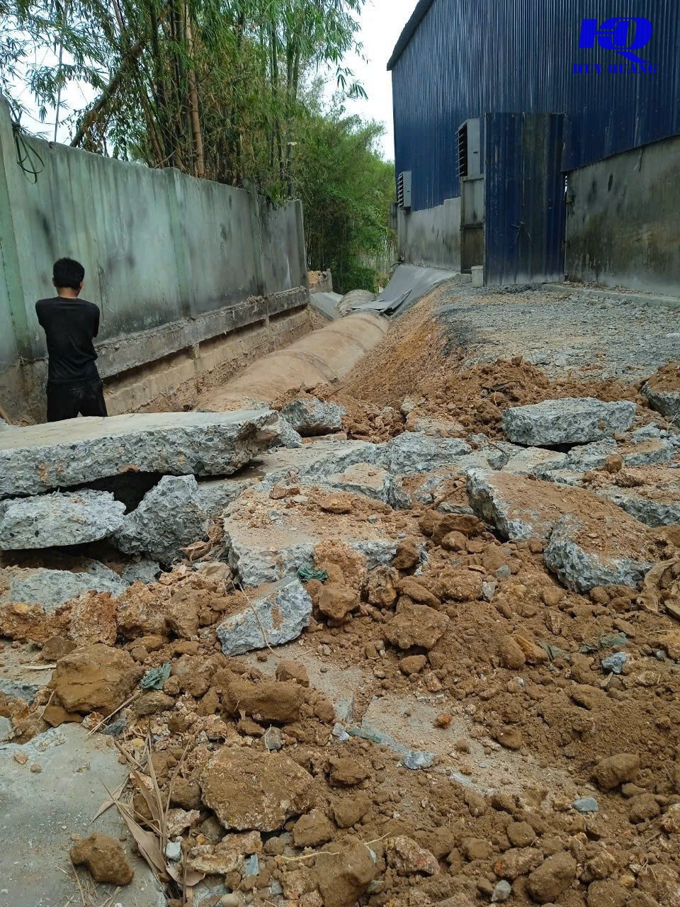 Đống bê tông vỡ sau khi đục phá nền, xếp dọc lối đi hẹp cạnh tường rào và nhà xưởng