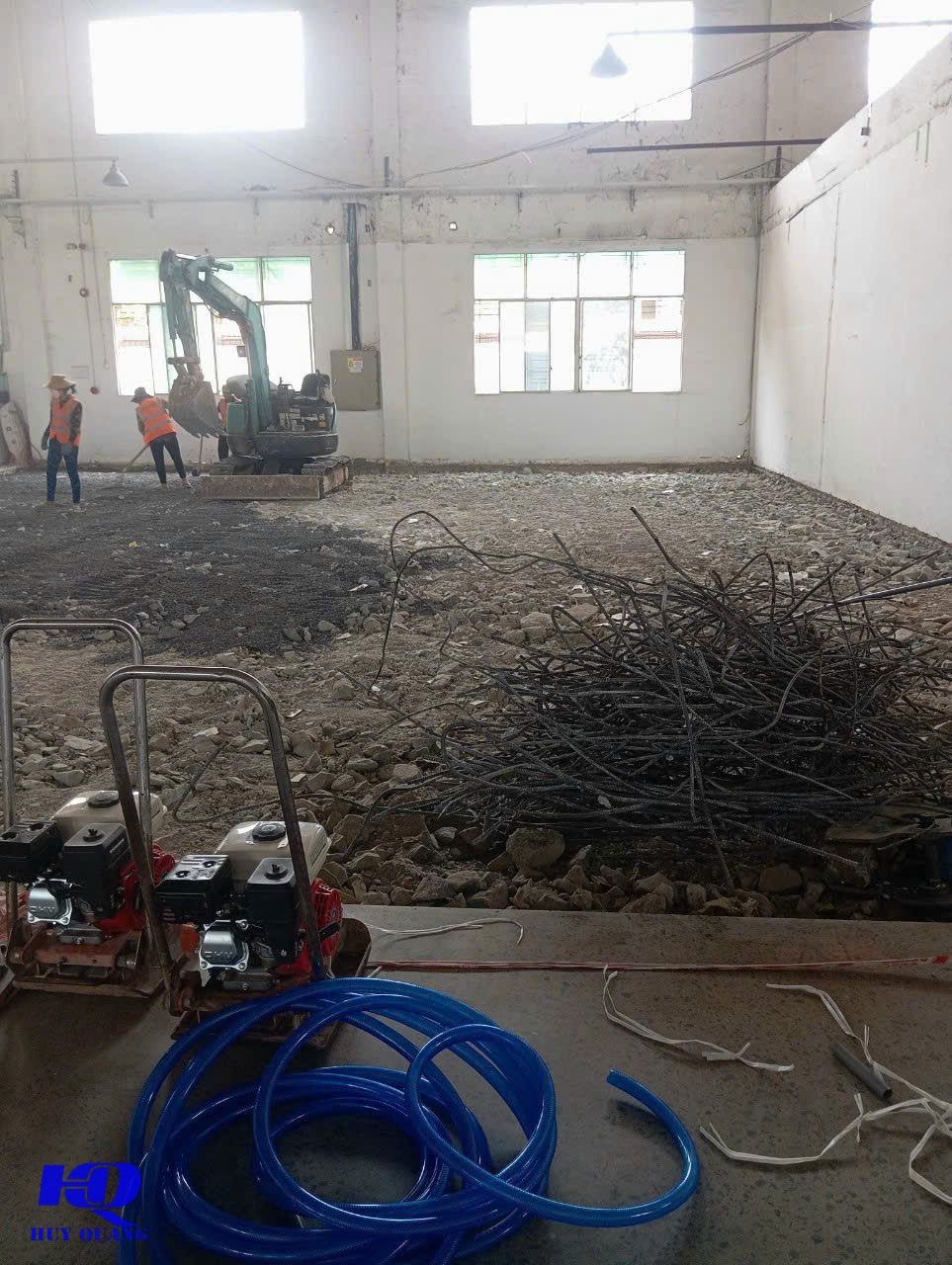 Nền nhà xưởng đã dọn dẹp mảnh bê tông và cốt thép cũ, vòi nước cuộn sẵn cạnh máy đầm, chuẩn bị mặt bằng cho hạng mục khoan lỗ kỹ thuật