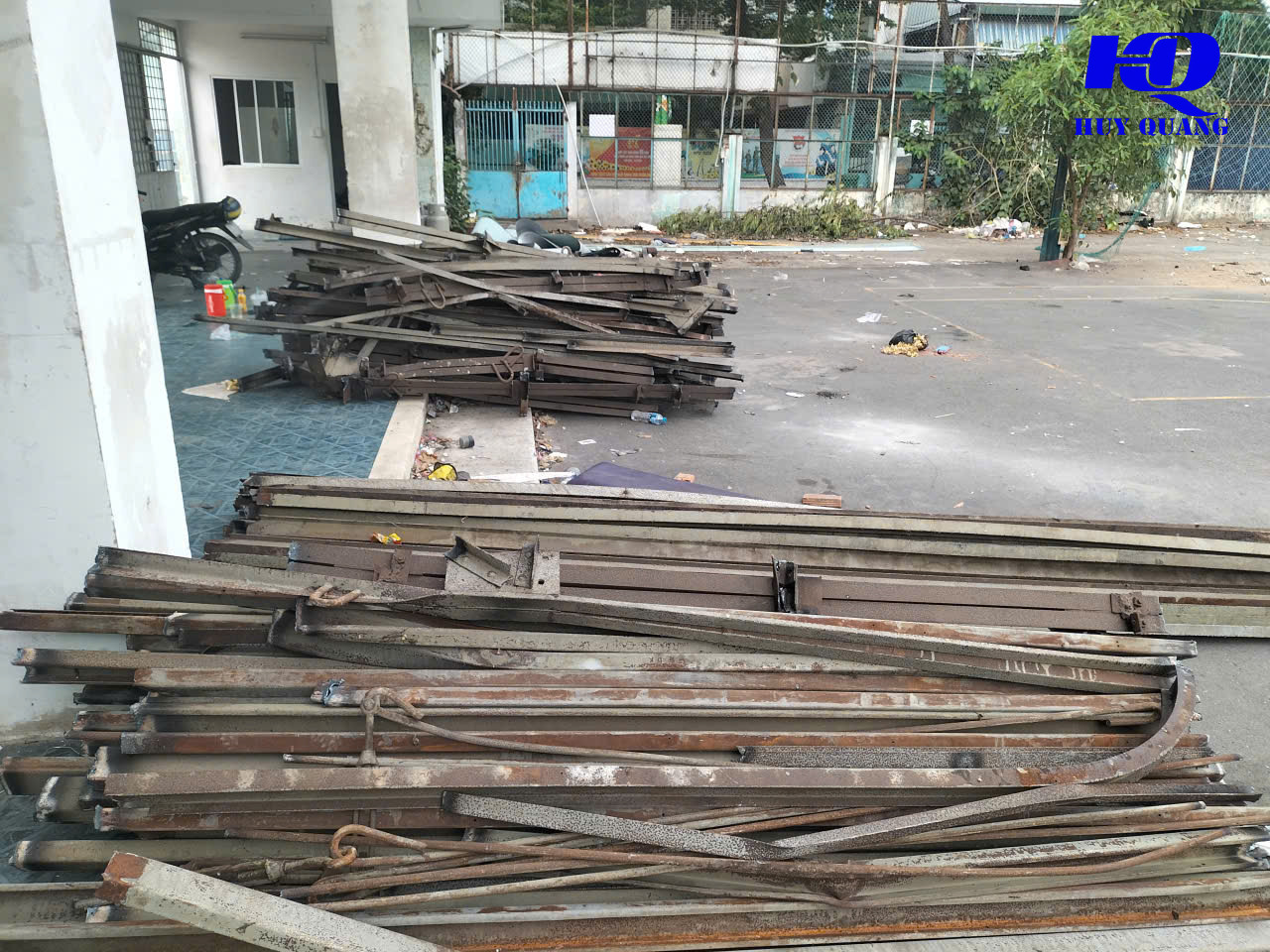 Hai đống thép hình, xà gồ và thanh sắt thu hồi xếp riêng trên sân bê tông cạnh hành lang tòa nhà