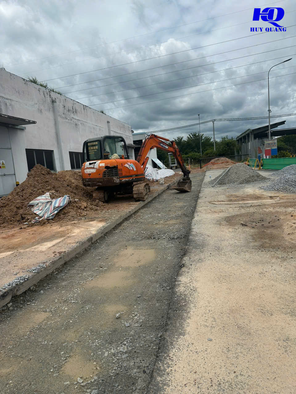 Máy đào xử lý nền bê tông cũ bên cạnh nhà xưởng, đá dăm tập kết sẵn để hoàn trả mặt bằng tại khu công nghiệp Bình Dương