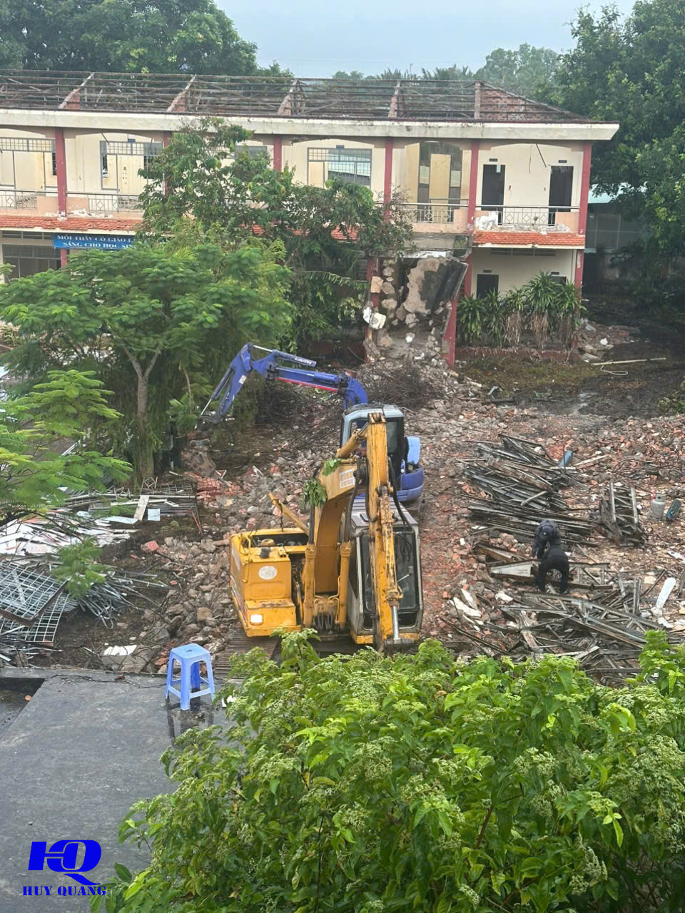 Máy đào bánh xích màu vàng phá tường dãy phòng học, sắt thép và khung cửa nhôm đã tháo xếp thành từng đống riêng